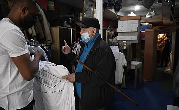 Betto Snay atiende a un comprador de la camiseta 'Cama de cartón' en su tienda de segunda mano.