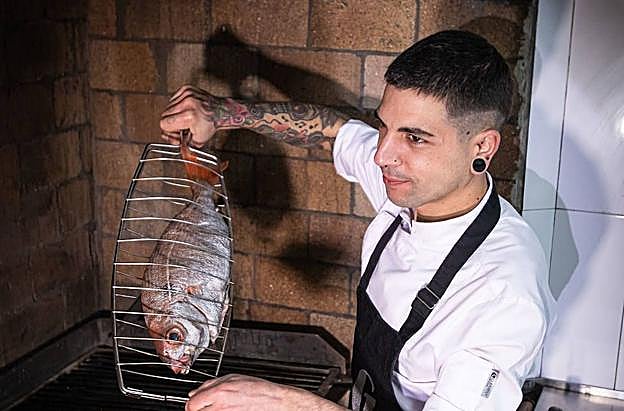 El cocinero se prepara para llevar al fuego en su rincón de Garena un besugo.