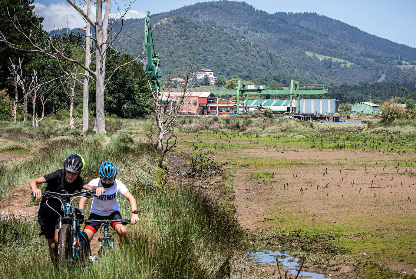 Dos jóvenes practican bici de montaña por los caminos junto a los astilleros de Murueta.