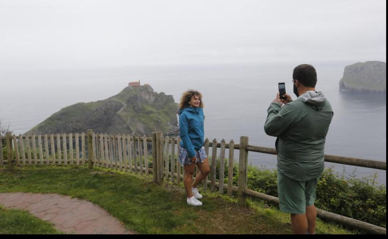 Una joven posa con la ermita de San Juan de Gaztelugatxe de fondo. 
