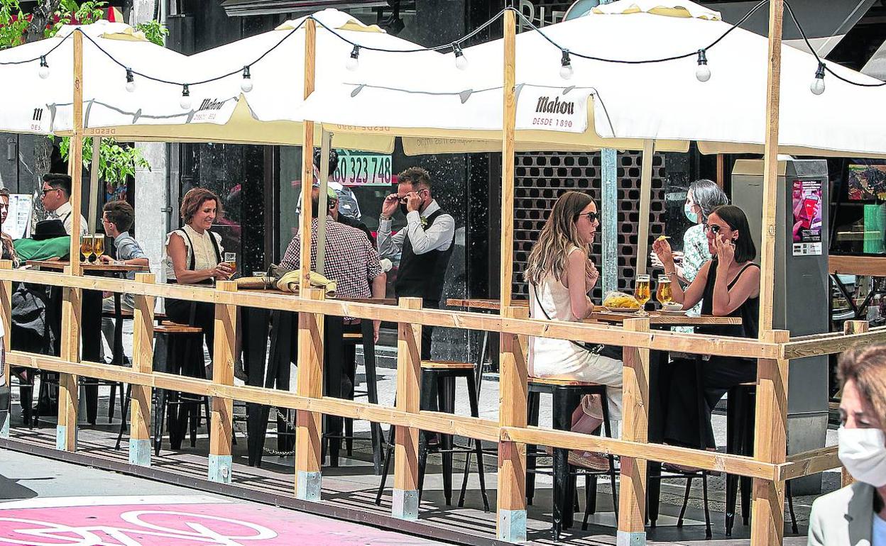 Varios grupos de clientes disfrutan de una terraza instalada sobre una zona de aparcamiento. 