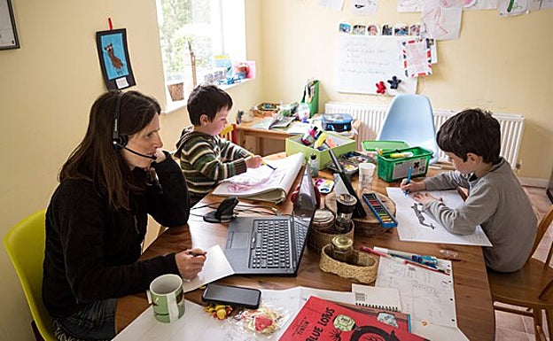 Una mujer teletrabaja al tiempo que se encarga del cuidado de sus dos hijos. 