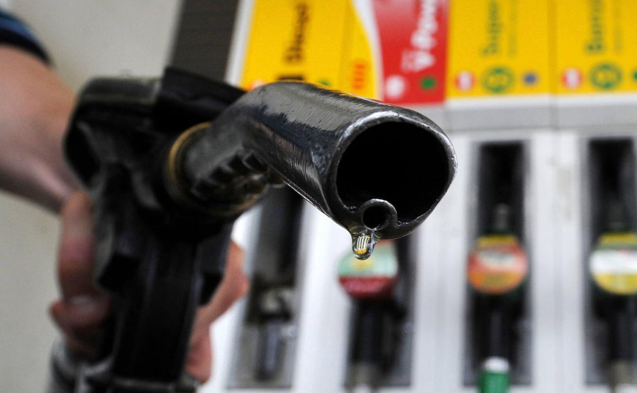 Un viajero sostiene un surtidor de gasolina en una estación de servicio. 