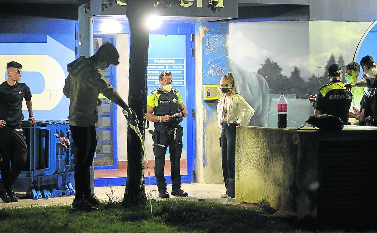 Un joven derrama la bebida en el jardín mientras la Policía Local de Barakaldo interpela a un grupo que estaba haciendo botellón. 