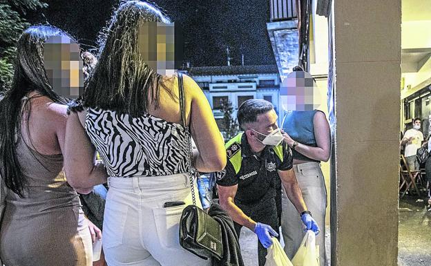 Un policía local requisa las bolsas de plástico con bebidas a un grupo de chicas. 