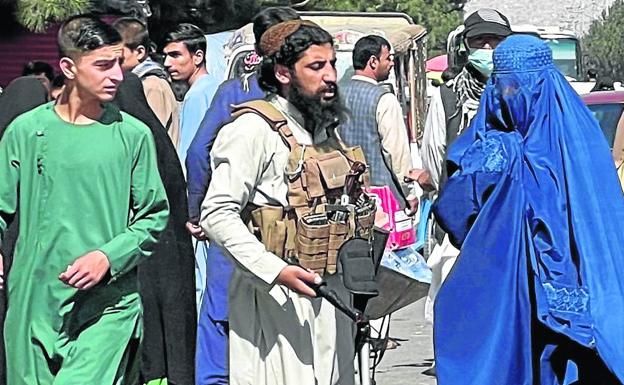 Fuerzas talibanes bloquean las carreteras alrededor del aeropuerto de Kabul, mientras pasa delante de ellos una mujer con burka. 