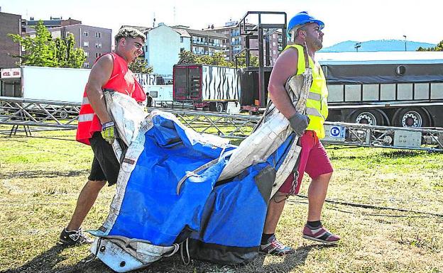 Dos operarios trasladan una lona. 