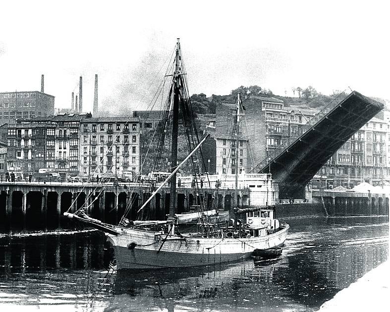 Carbonero pasando bajo el puente del Ayuntamiento. Al fondo, las chimeneas de la fabrica de Echevarría. 