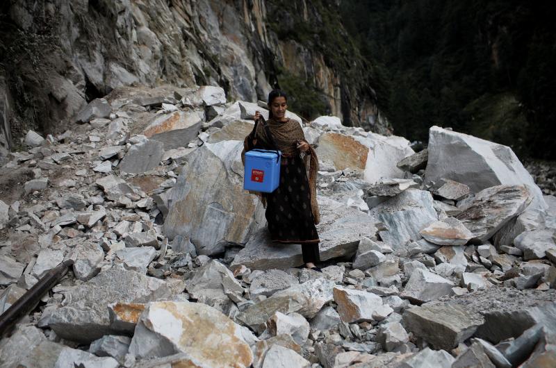 Su compañera, Kanta Devi, de 26 años, camina por una carretera que fue bloqueada después de un deslizamiento de tierra. Este incidente les obligó a dejar el todoterreno aún más lejos de su destino, escalar el muro y luego caminar hasta el comienzo del sendero que conduce a la aldea.