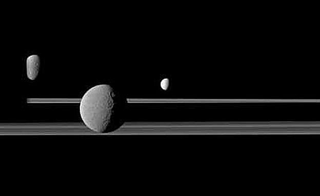 Dione, Rhea y Encélado (de izquierda a derecha), en la cara nocturna de Saturno (el planeta está a la izquierda) y 'flotando' sobre los anillos. 