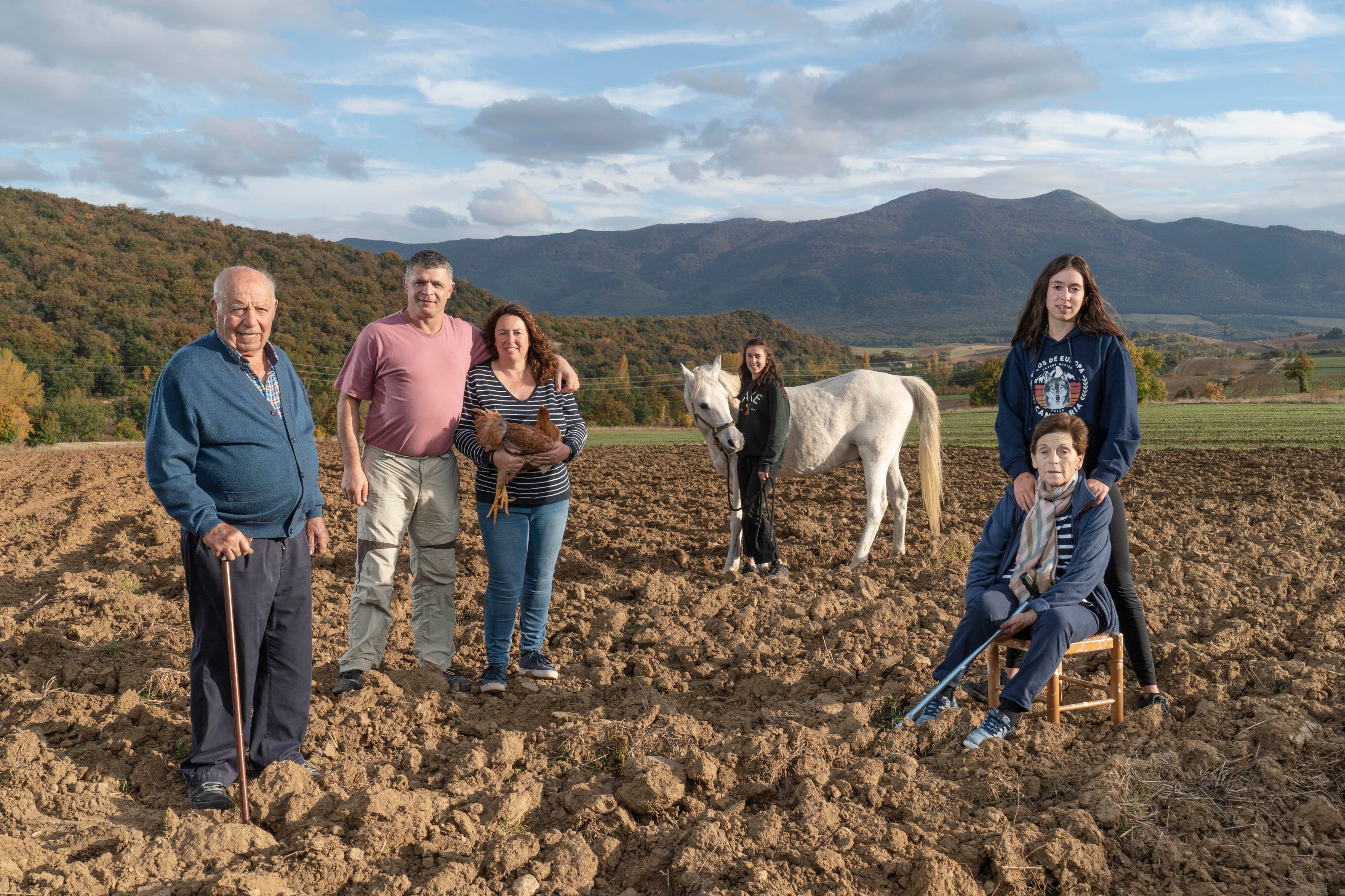 La familia Díaz López de Lacalle retratada en una de sus fincas, en Antoñana. José Luis, el abuelo mira al frente, apoyado en su cachava. A su lado, José Ignacio y Tamar, que sujeta entre los brazos uno de los pollos lumagorri que cría. Eneritz acompaña a su abuela, María Pilar, sentada en una banqueta. Al fondo, su hermana Uxue acaricia a Kuki, el caballo de la familia.