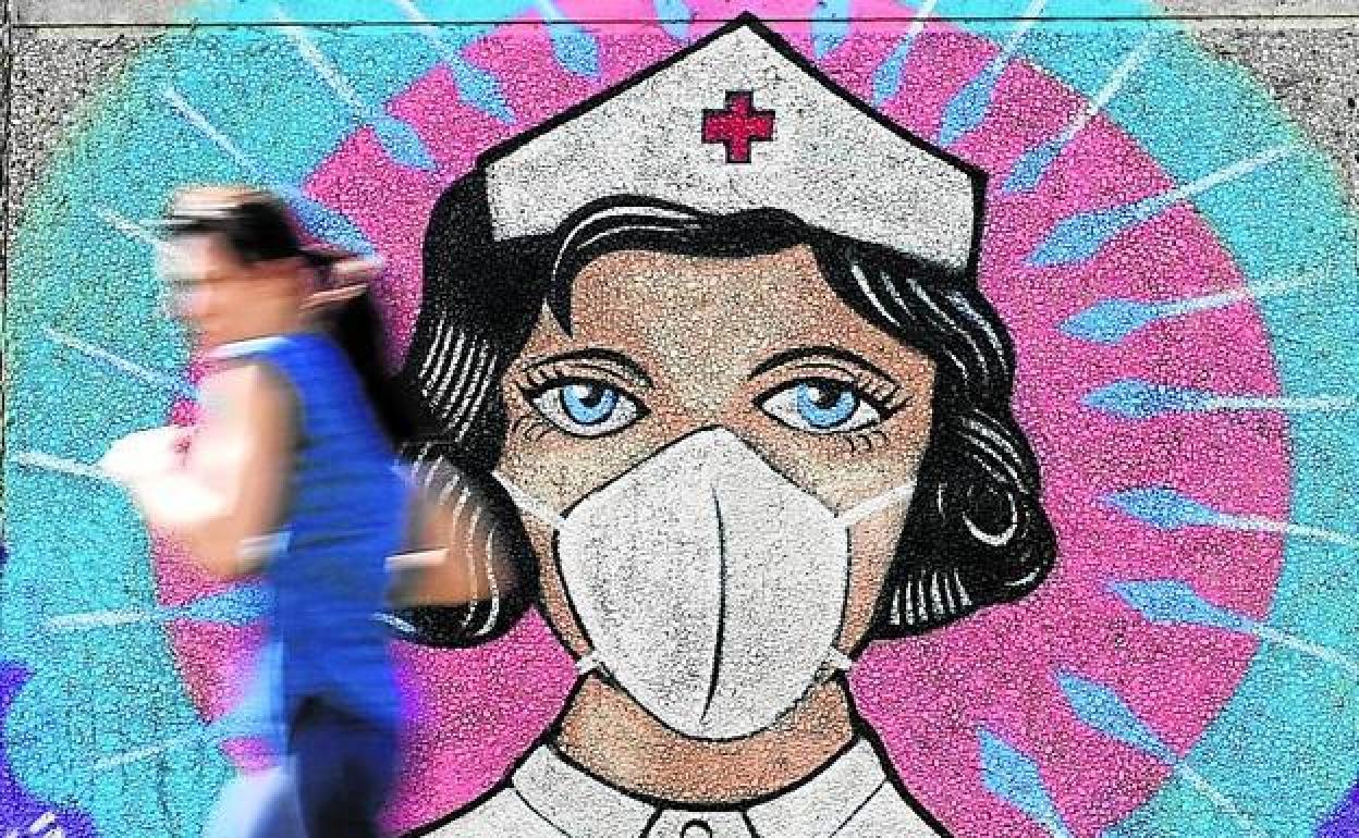 Una mujer junto a un mural dedicado a las enfermeras.