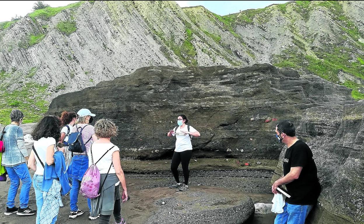 Las escorias de hierro que las mareas han acercado a Azkorri han llegado a formar hasta rocas, como explica Bárbara Casas a varios visitantes. 