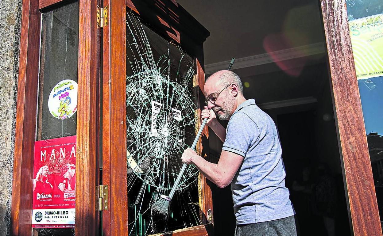 Un vecino limpia los cristales rotos en uno de los portales de Bilbao afectados por los altercados. 