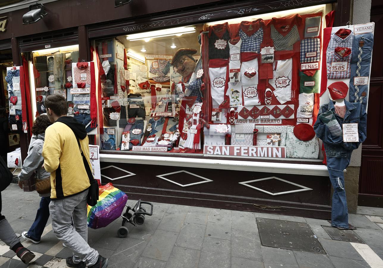Un grupo de personas pasan junto a una tienda con la ropa típica de los Sanfermines en el escaparate. 