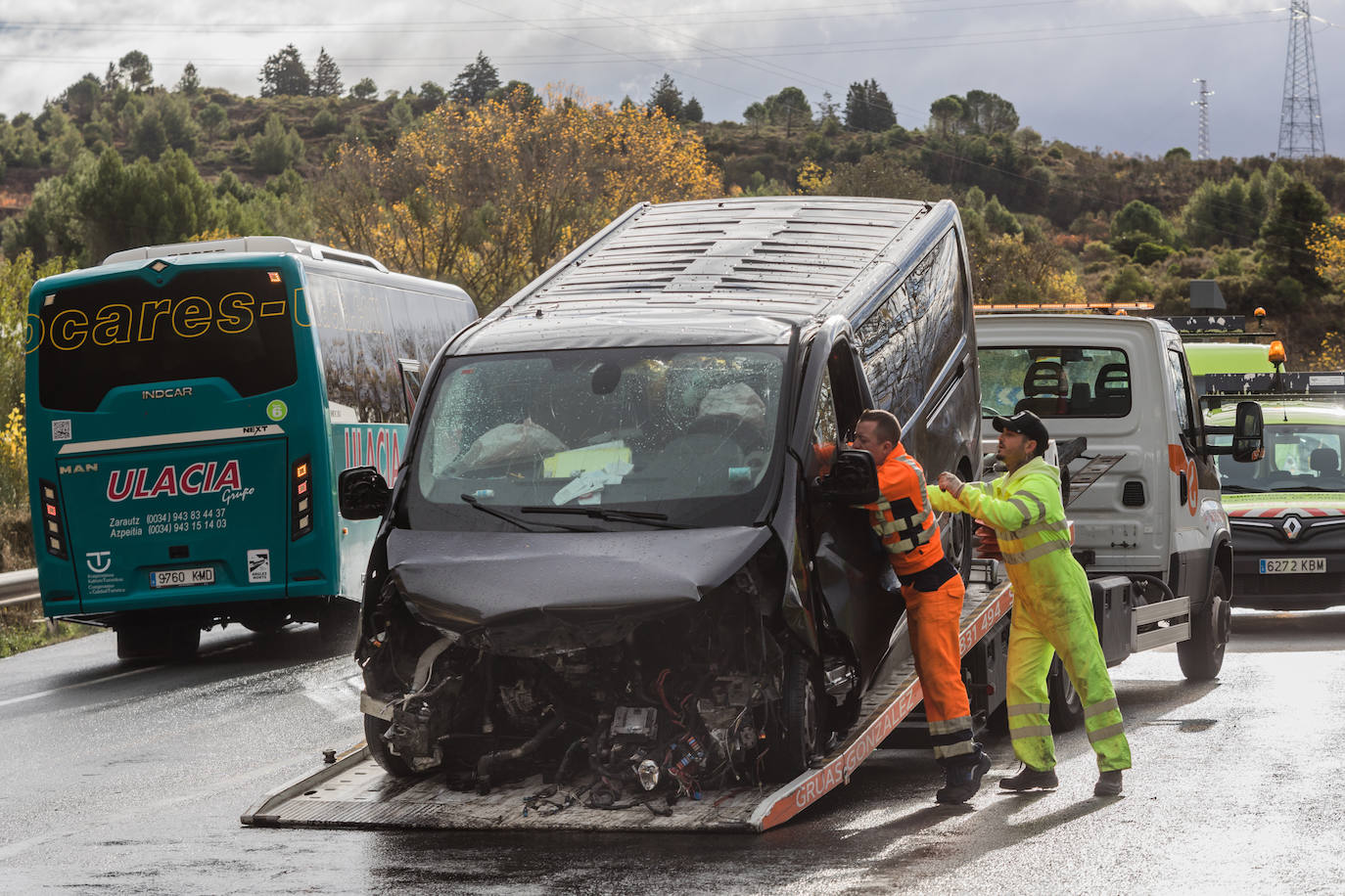 Dos operarios suben la furgoneta accidentada a una grúa.