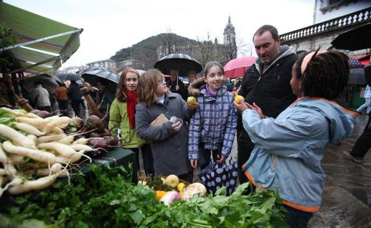 Alejandro Arrieta enseña las frutas de su puesto a varias niñas en la última feria de Lekeitio. 