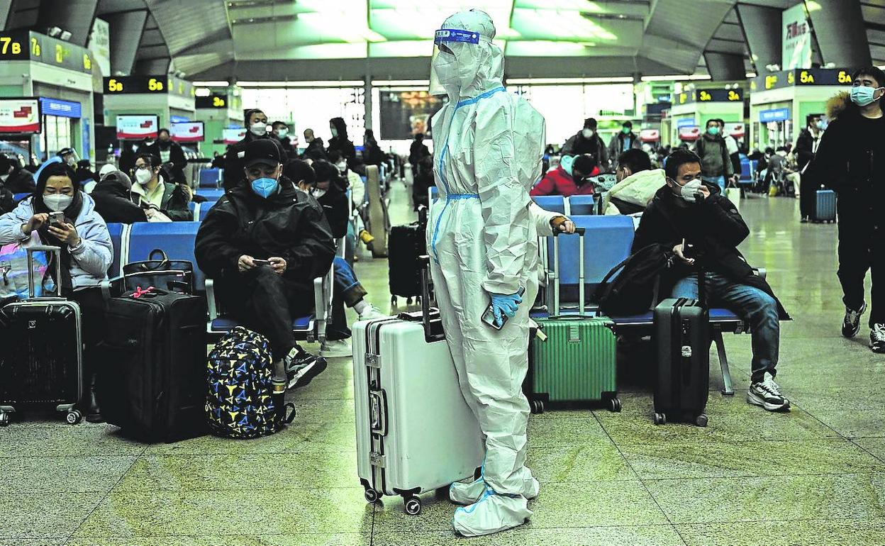 Un pasajero espera su vuelo en el aeropuerto de Pekín vestido con un traje de seguridad.