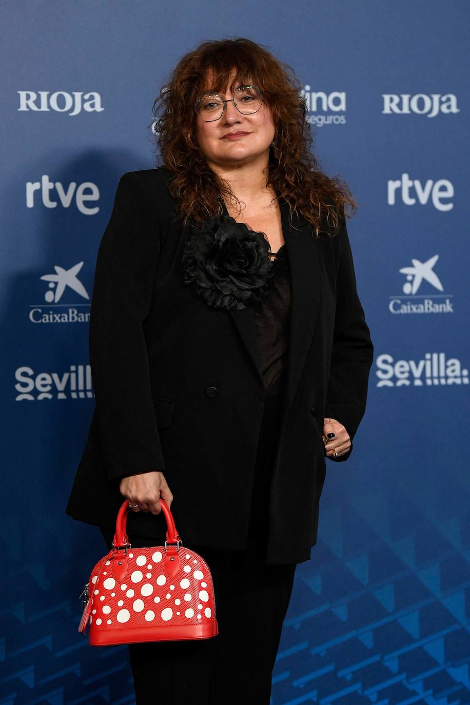 La directora Isabel Coixet escogió un traje negro con una gran flor en la solapa. El toque inesperado y original lo consiguió con este bolso rojo con lunares blancos de Louis Vouitton by Yayoy Kusama.