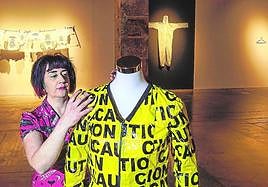 Edurne Herrán coloca un vestido de precintos de precaución. Detrás, prendas con datos, alusiones al covid y al traje del emperador