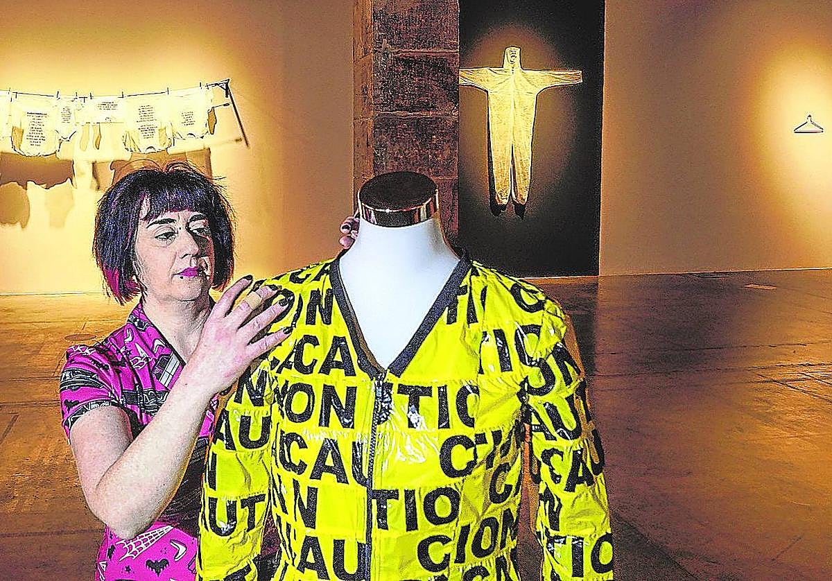 Edurne Herrán coloca un vestido de precintos de precaución. Detrás, prendas con datos, alusiones al covid y al traje del emperador