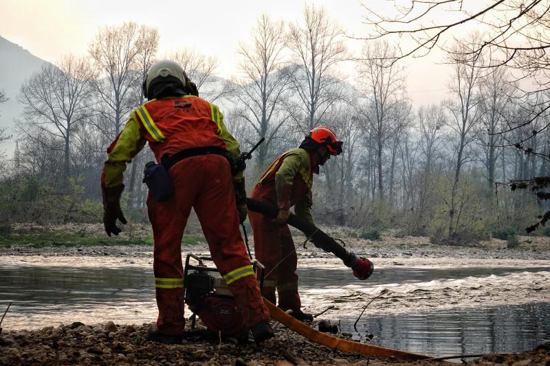 Un equipo de bomberos carga agua en un río cercano a un foco