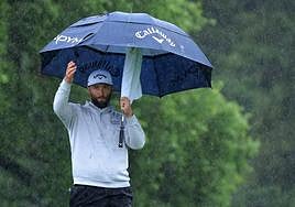 Jon Rahm golpea la bola desde el tee rodeado de aficionados con paraguas para protegerse de la lluvia.