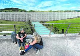 Una pareja se toma un aperitivo mientras espera su vuelo en la zona exterior de Salidas, con el aparcamiento principal del aeropuerto al fondo.