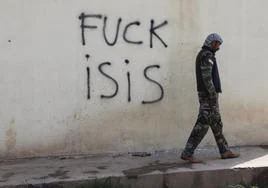 Un miliciano kurdo camina junto a un grafiti contra el Estado Islámico en Dibisi.