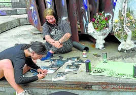 Amigos pintan carteles para adornar una plaza en la que desde hace una semana destacan las velas y flores en honor de Erlantz, el joven arrollado por un tren.