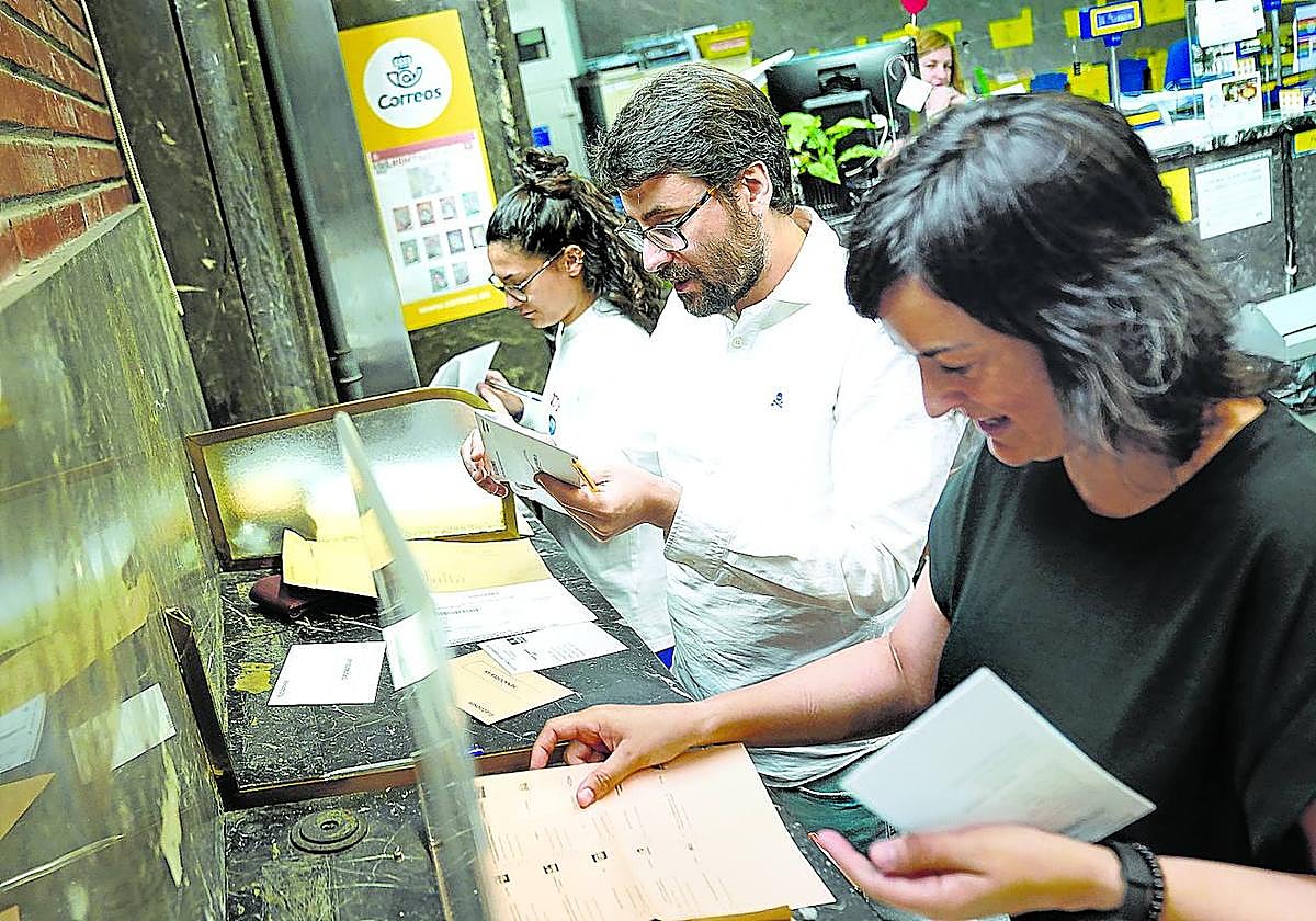 Tres ciudadanos completan sus trámites de votación en la oficina central de Correos de Bilbao.