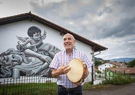 Julián Mari toca la pandereta ante el grafiti de su caserío.