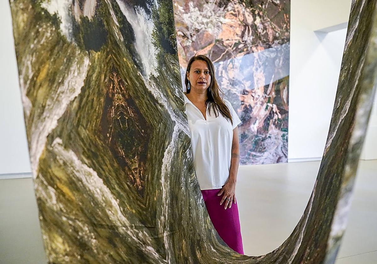 La artista colombiana afincada en California Carolina Caycedo, junto a su retrato de un río y la pieza 'Tierra de amigos', al fondo, que bautiza a la exposición en el Museo Artium.