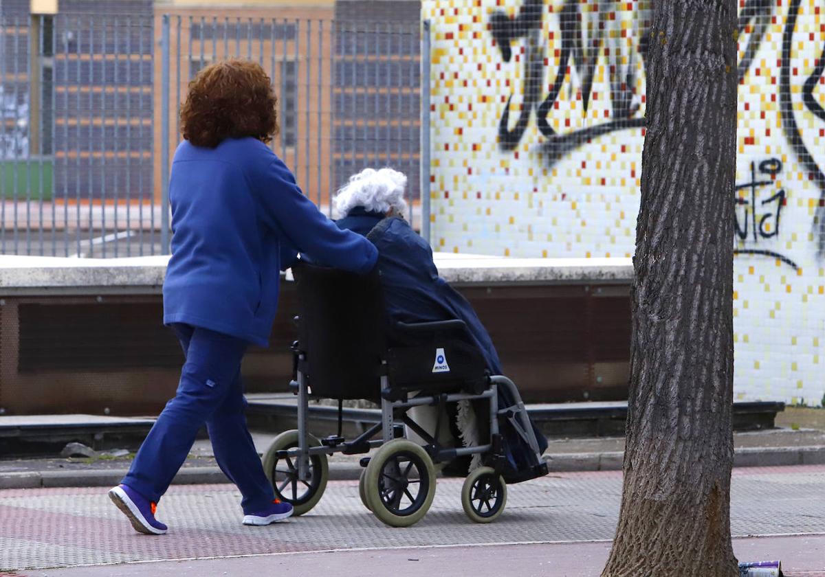 Una persona cuida de un mayor en silla de ruedas