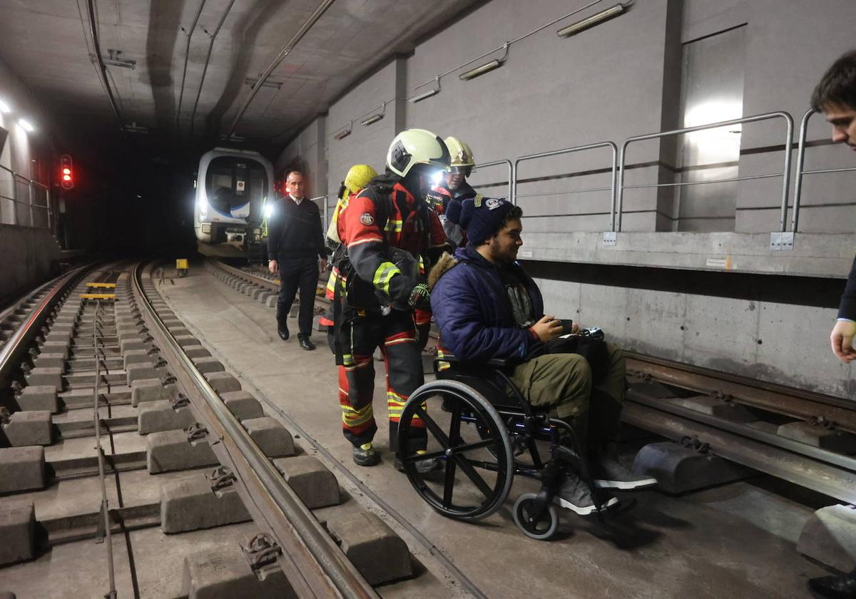 Los bomberos evacuan por las vías a un joven en silla de ruedas.