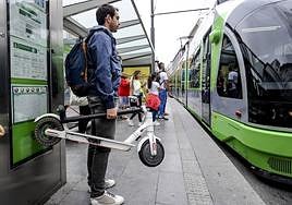 Un usuario con un patinete en una parada del tranvía.
