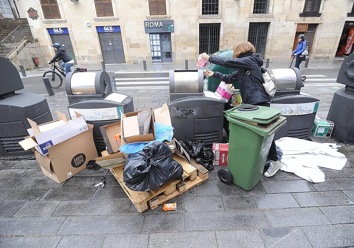 Una vecina se esfuerza para conseguir tirar la basura en los contenedores rebosantes en plena Virgen Blanca, la postal de Vitoria.