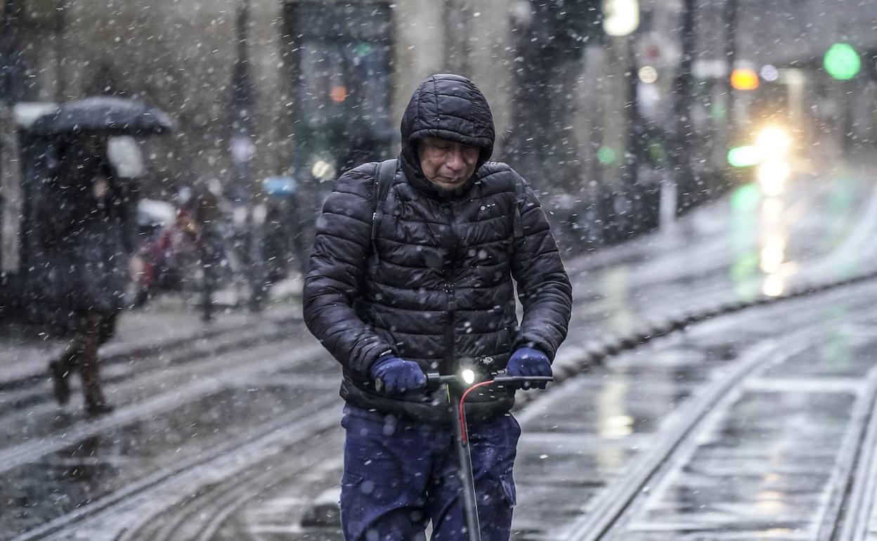 Un hombre circula con su patinete por General Álava bajo la nieve. 