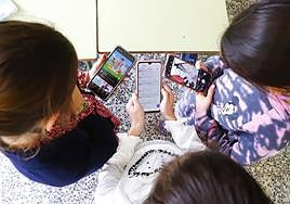Tres menores con sus teléfonos móviles en un aula.