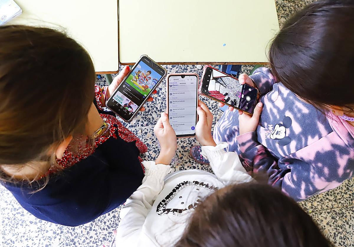 Tres menores con sus teléfonos móviles en un aula.
