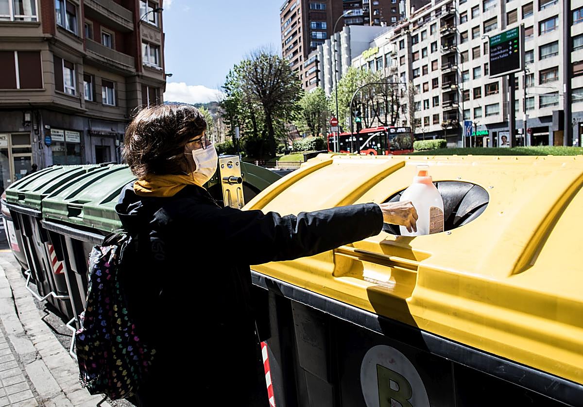 Una mujer deposita un envase de plástico en un contenedor amarillo.