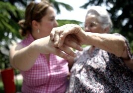 Una mujer con dependencia sujeta la mano de su cuidadora.