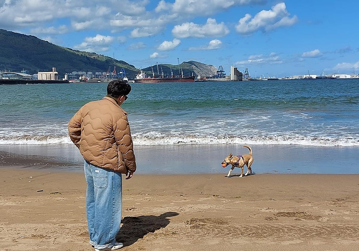 Una chica juega con su perro en la playa de Ereaga.