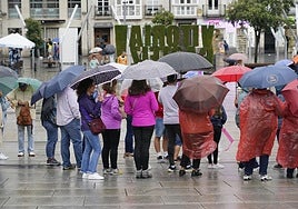 Varias personas se protegen de la lluvia en la plaza de la Virgen Blanca.