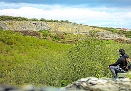 Un joven sentado observa el paisaje con la mina de Nanclares en el horizonte.