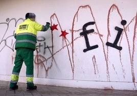 Un empleado municipal limpia una pintada antigua.