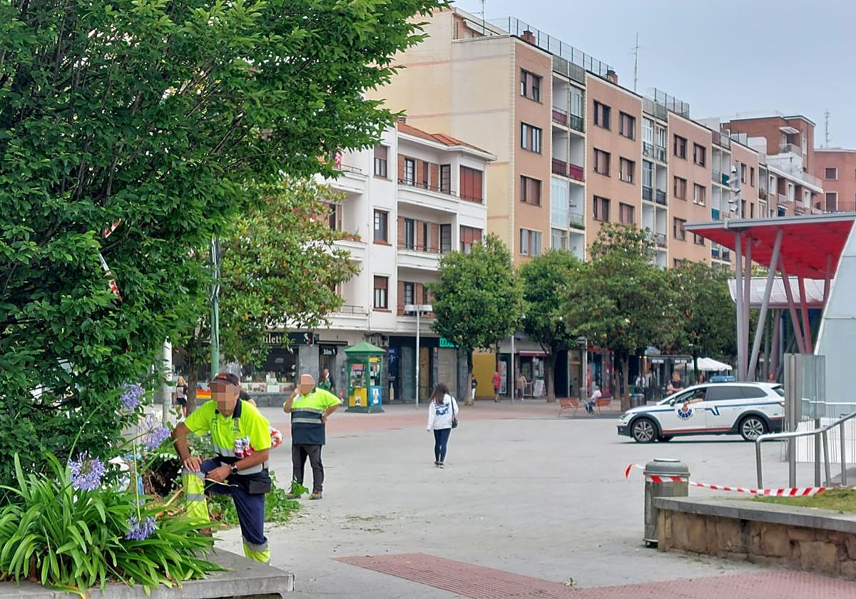 Dos operarios de jardinería en la plaza de la estación del metro de Algorta con un coche patrulla de la Ertzaintza a escasos metros.