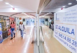 Dos mujeres pasan por el pasillo central de las galerías Itaca, donde se aprecian lonjas vacías.