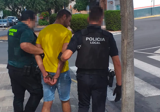 Un guardia civil y un policía trasladan al detenido a un coche patrulla.