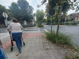 Una vecina de Neguri pasea por una acera donde la vegetación lleva tiempo sin mantenimiento.